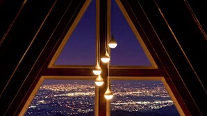 Uitzicht door een driehoekig raam, met drie hanglampen, op een stadszicht in de nacht.