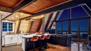 Een moderne keuken met een centraal eiland, een eetgedeelte met barstoelen en een groot raam met uitzicht op de stad.