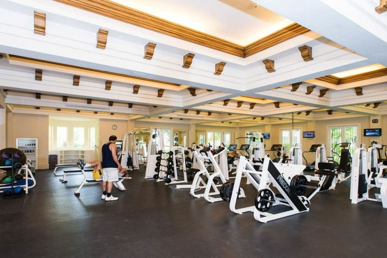 Un gimnasio con diversos equipos de ejercicio, incluyendo máquinas de pesas y pesas libres, y una persona entrenando.