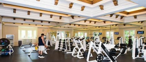 A gym with various exercise equipment, including weight machines and free weights, and a person working out.