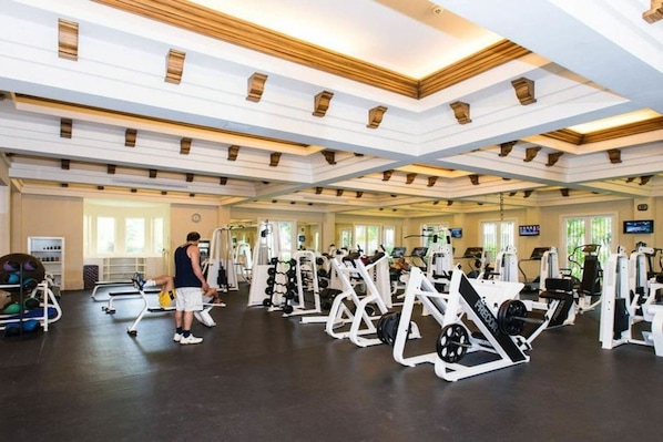 A gym with various exercise equipment, including weight machines and free weights, and a person working out.