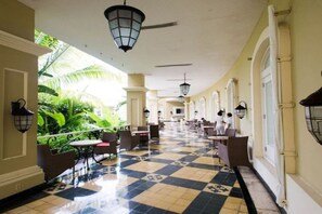 A corridor with a checkered floor, tables, chairs, and hanging lanterns.