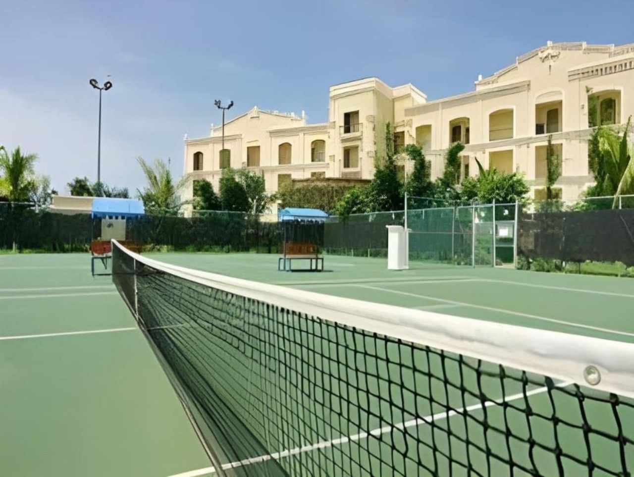 Una cancha de tenis con una red, rodeada por una valla, y un edificio al fondo.