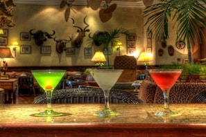 A bar area with three martini glasses on a counter, a patterned chair, and a wall with mounted animal skulls.