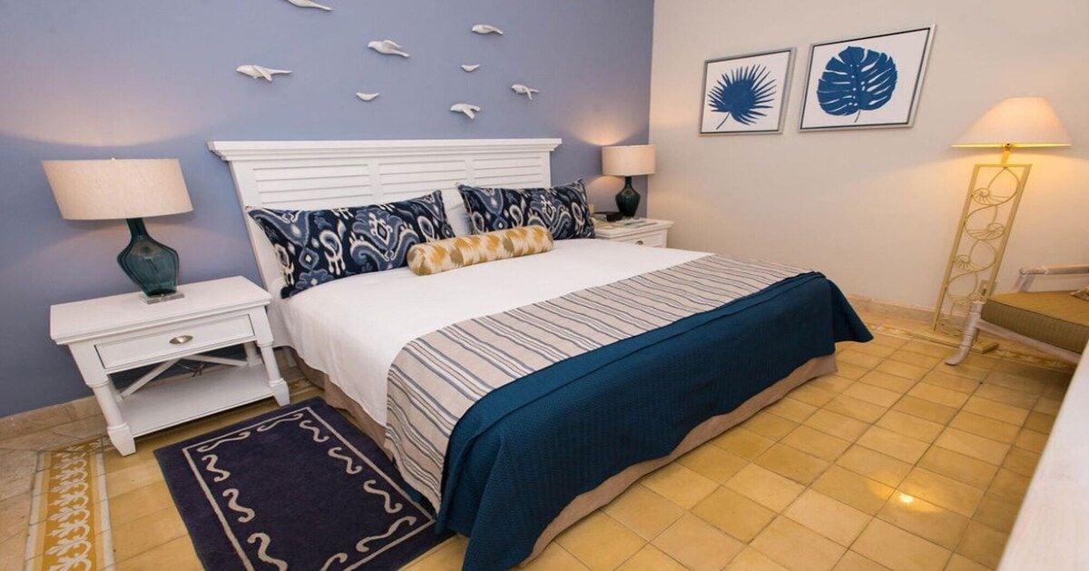 A bedroom with a bed, nightstands, a lamp, a rug, and wall art.
