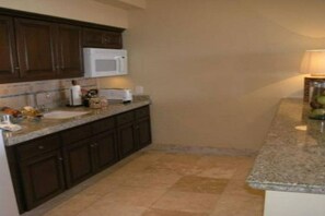 A kitchen with dark wooden cabinets, a white microwave, and a granite countertop.