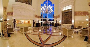 A grand lobby with a central circular floor design, a large chandelier, and classical decor.