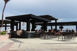 An outdoor seating area with tables and chairs, a covered structure, and a view of the sea.