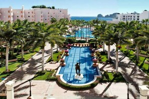 A resort with a central swimming pool, palm trees, and a view of the sea.