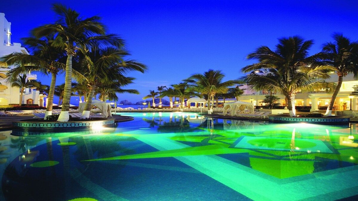 A pool area with palm trees, a clear sky, and a building in the background.
