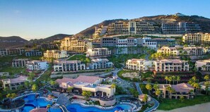 A resort with multiple buildings, a large swimming pool area, and a hilly backdrop.