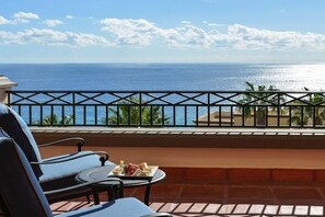 A balcony with a view of the ocean, a table with food, and two chairs.