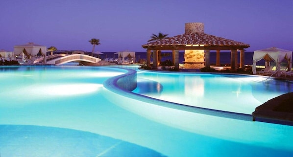 A swimming pool with a curved design, a gazebo, and lounge chairs.