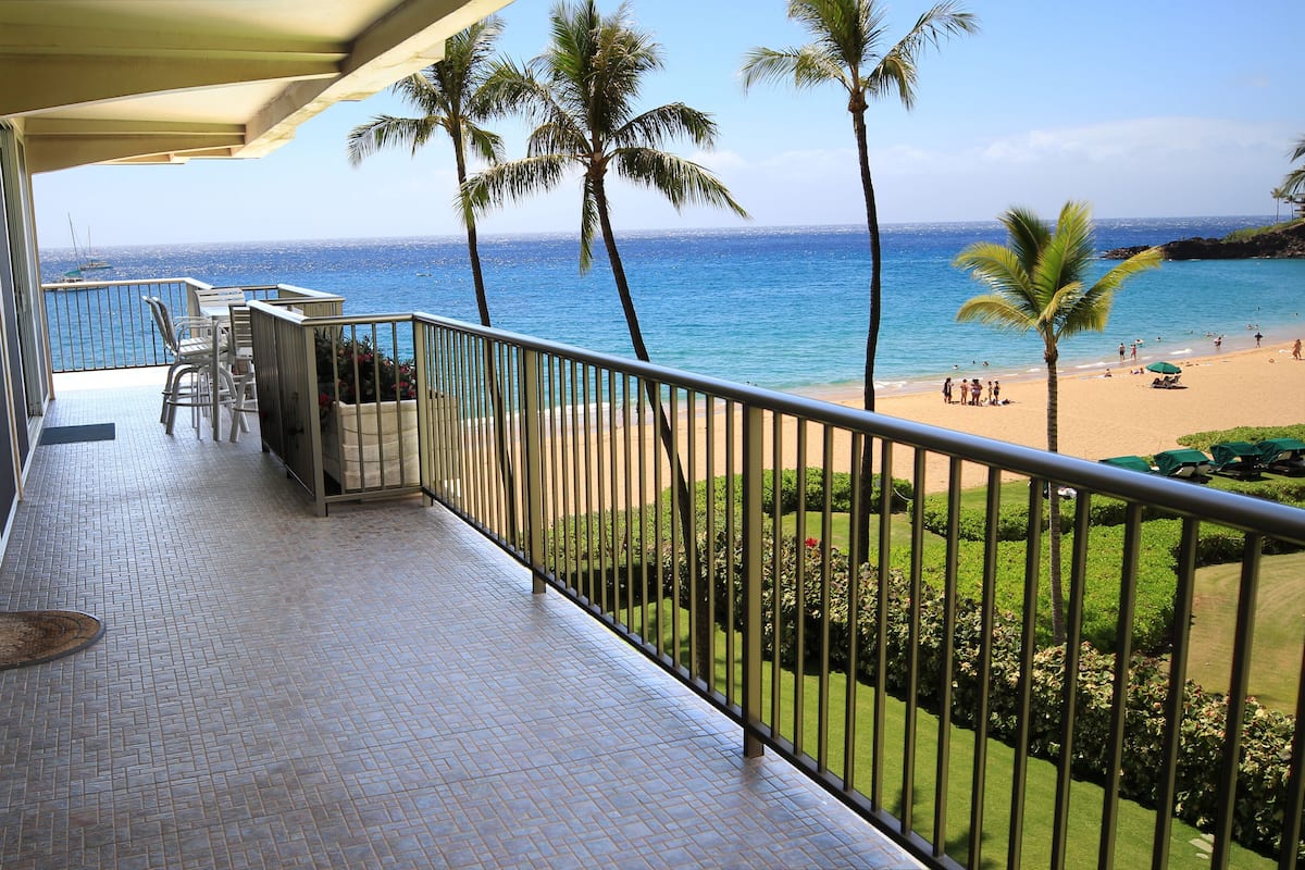 Un balcon avec vue sur la plage, les palmiers et un ciel bleu azur.