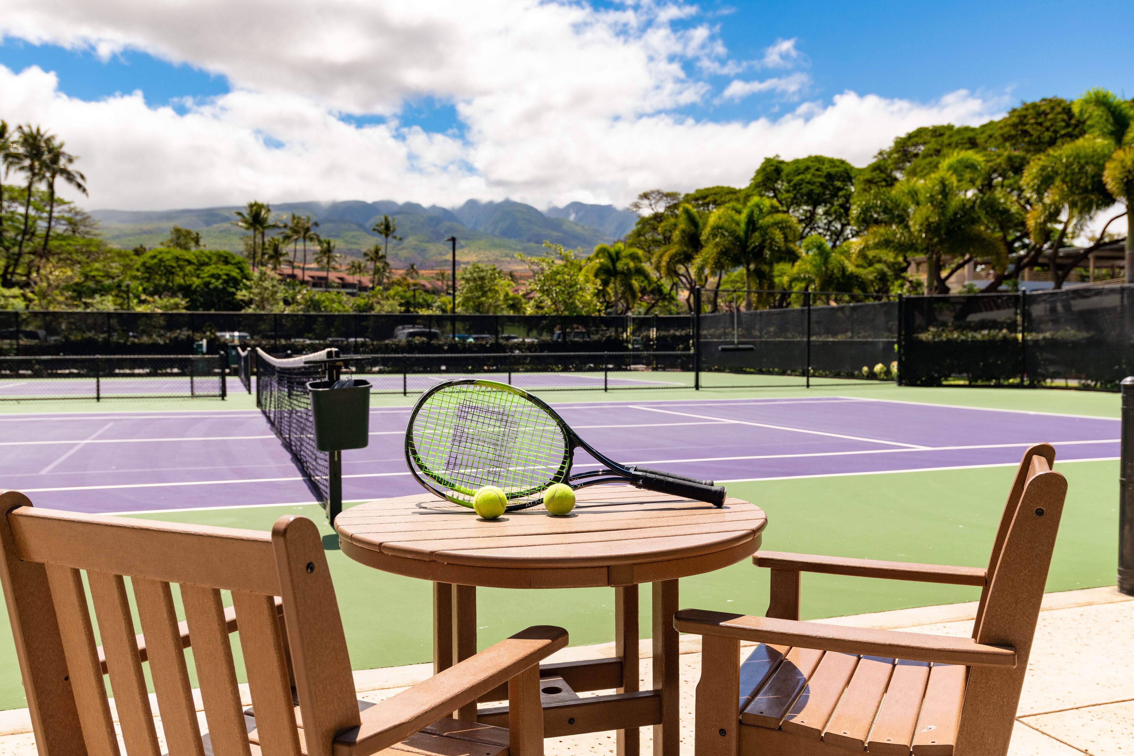 Una cancha de tenis con mesa y sillas, raquetas y pelotas.