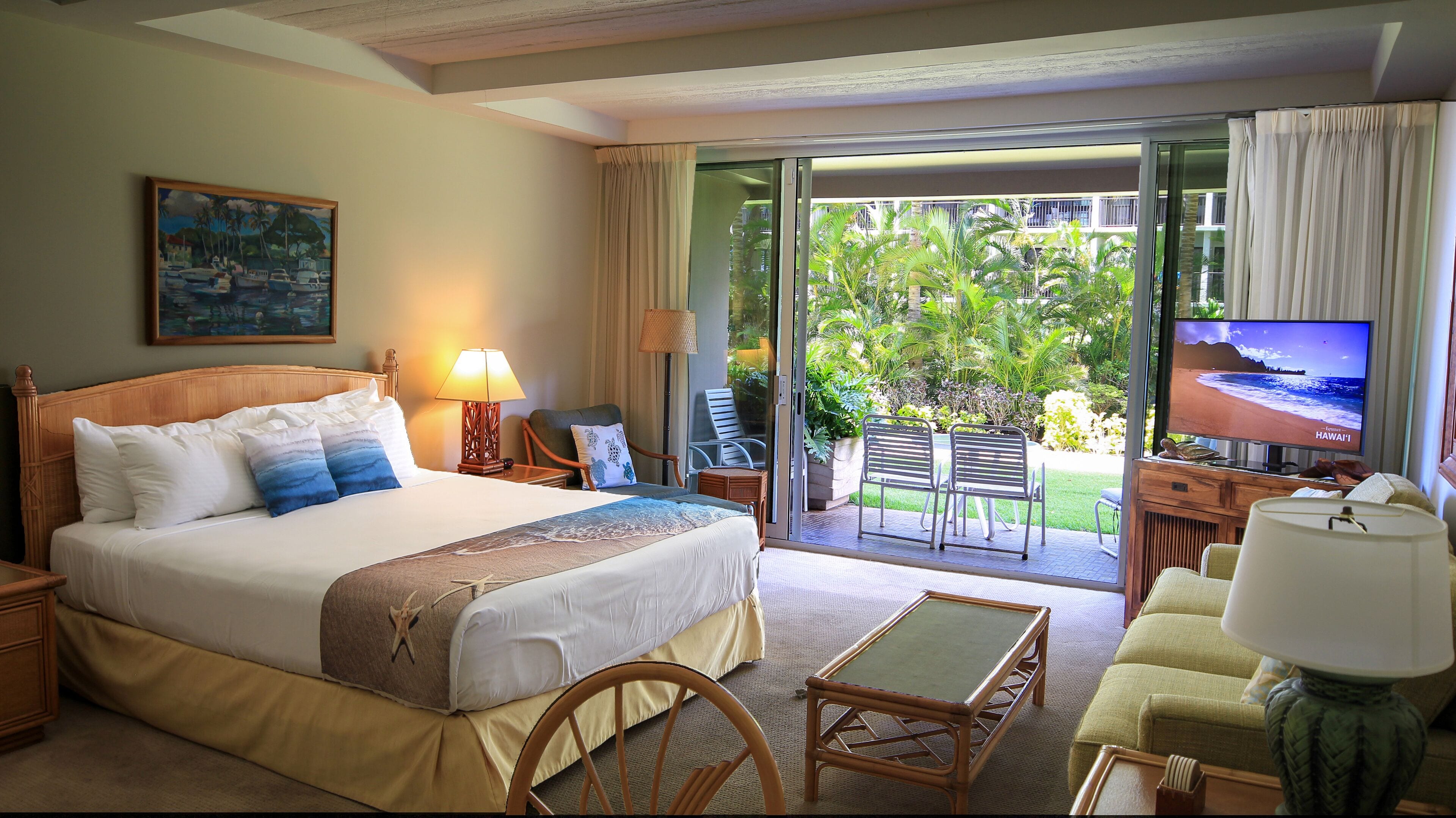 Quarto de hotel com cama grande, televisão, escrivaninha e varanda com vista para o exterior.