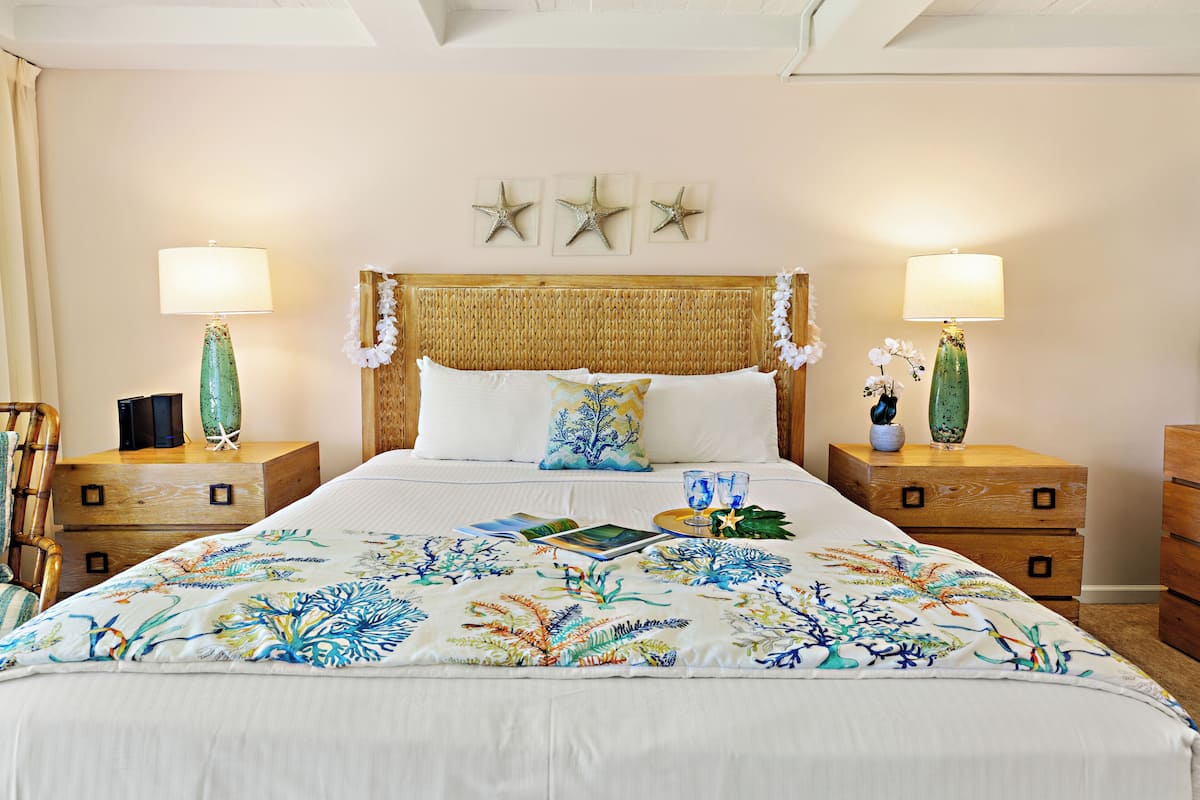 Un lit bien fait, recouvert d’une couvre-lit à motifs floraux, deux tables de chevet avec des lampes et trois décorations murales en forme d’étoiles de mer.