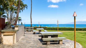An outdoor patio area with stone flooring, picnic tables, and a view of the ocean.