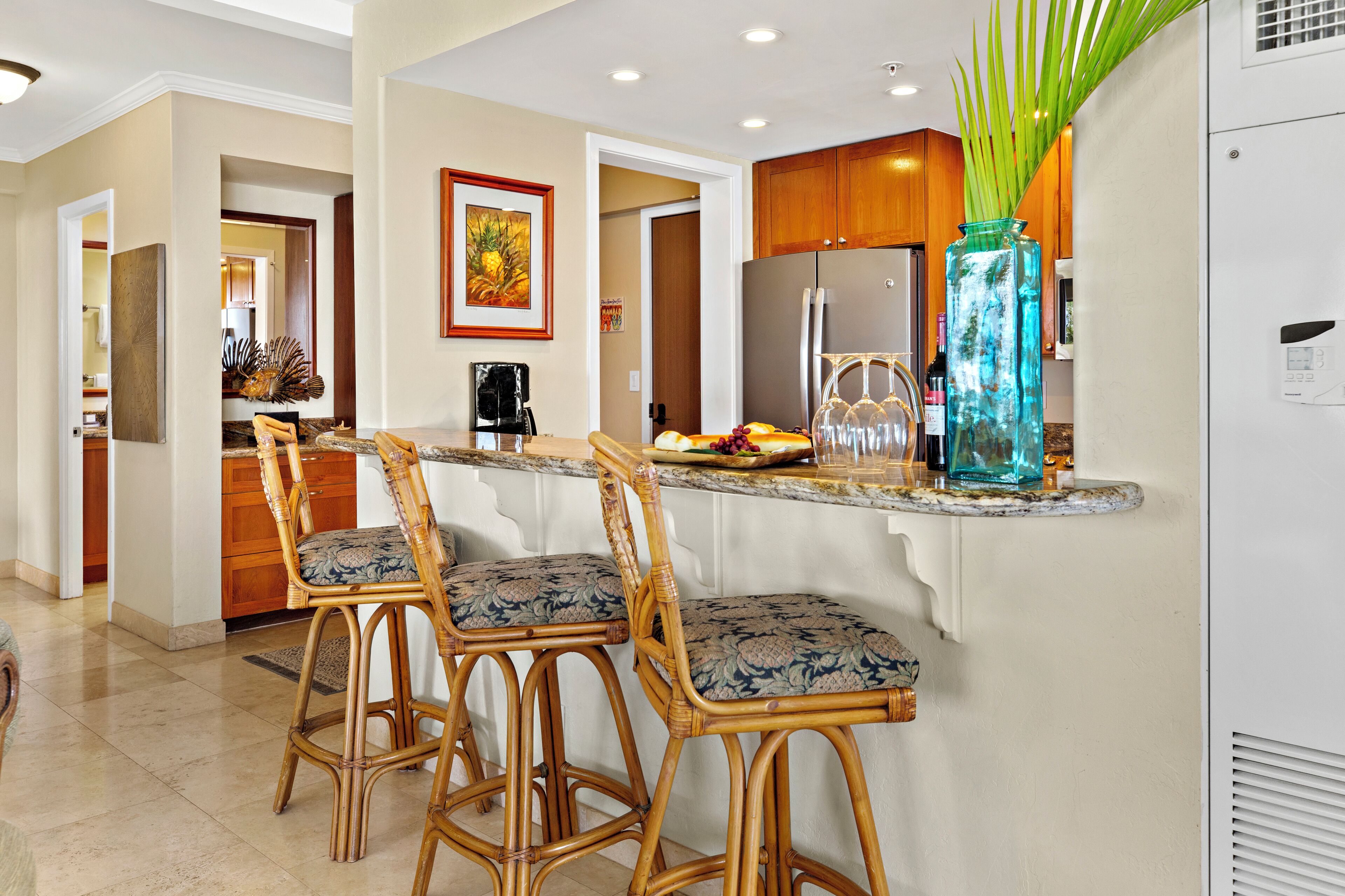 A kitchen with a bar area, wooden cabinets, and a large vase with green leaves.