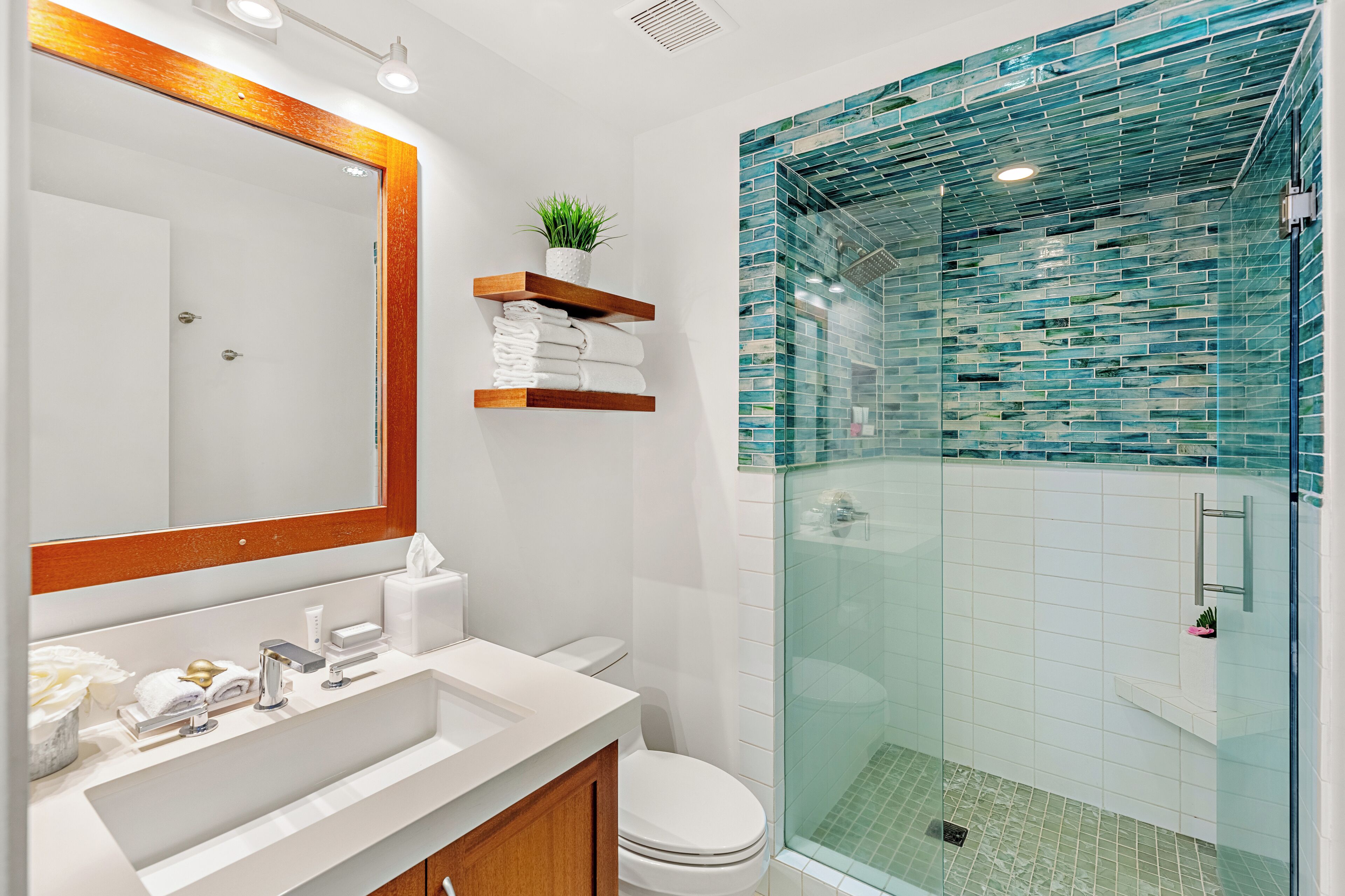 Un baño moderno con ducha envuelta en vidrio, un lavamanos blanco con tocador de madera y un espejo con marco de madera.