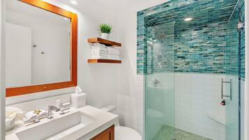 Un baño moderno con ducha envuelta en vidrio, un lavamanos blanco con tocador de madera y un espejo con marco de madera.