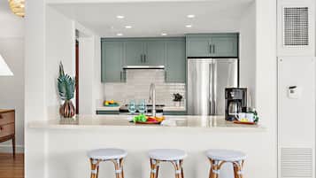 A modern kitchen with teal cabinets, stainless steel appliances, and a central island with bar stools.