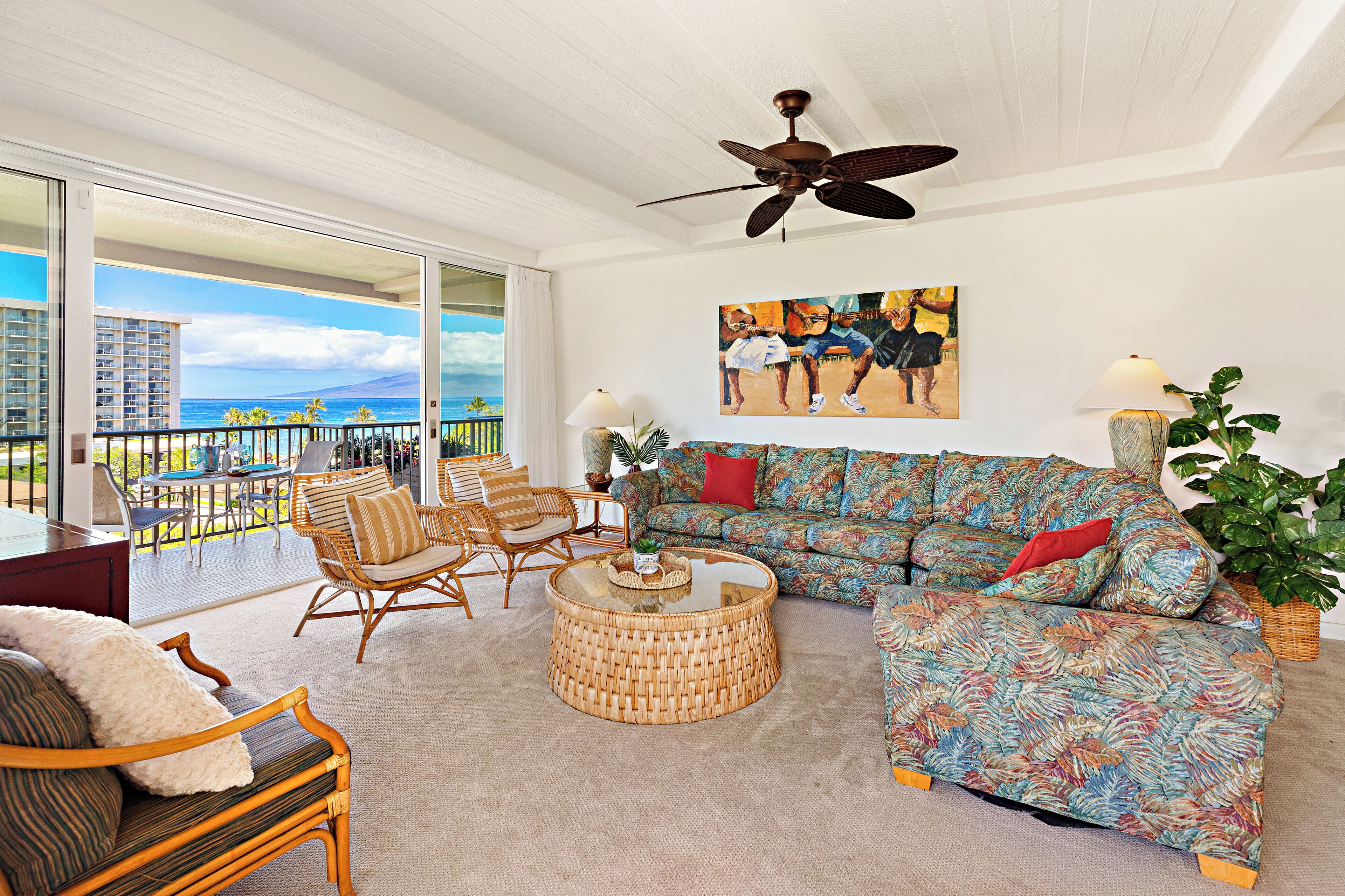 A spacious living area with a balcony, wicker furniture, a colorful sofa, and a ceiling fan.