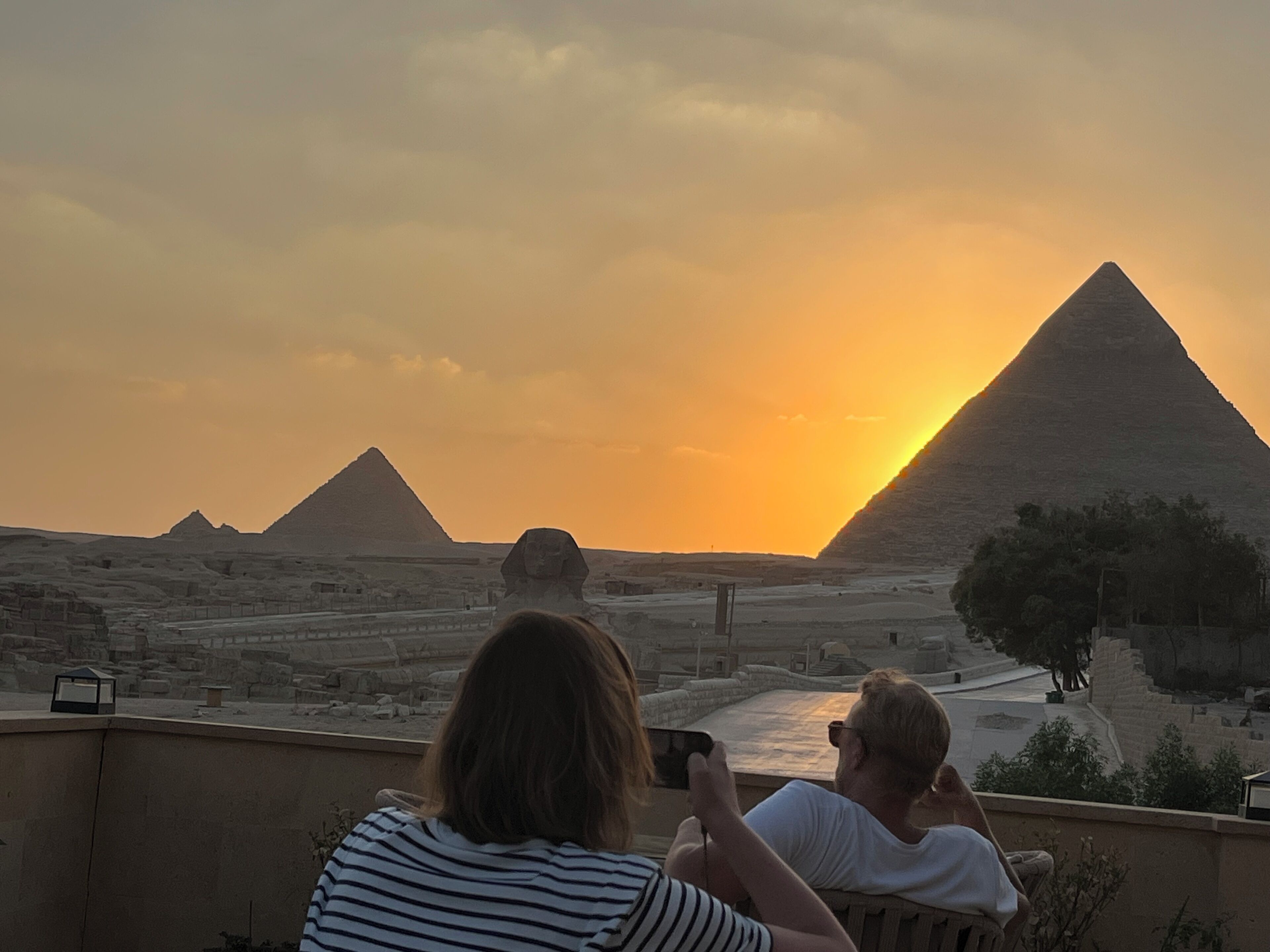 A view of the pyramids at sunset with tourists observing.
