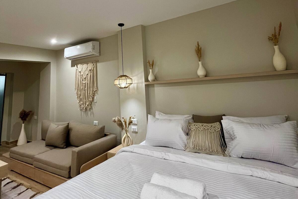 A modern hotel room with a large bed, a sofa, and a small seating area.