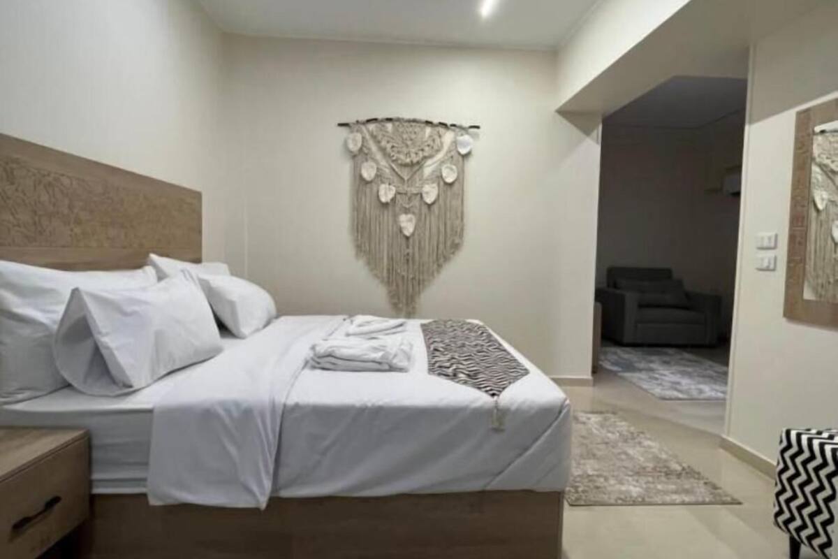 A modern bedroom with a wooden bed, a decorative wall hanging, and patterned rugs.