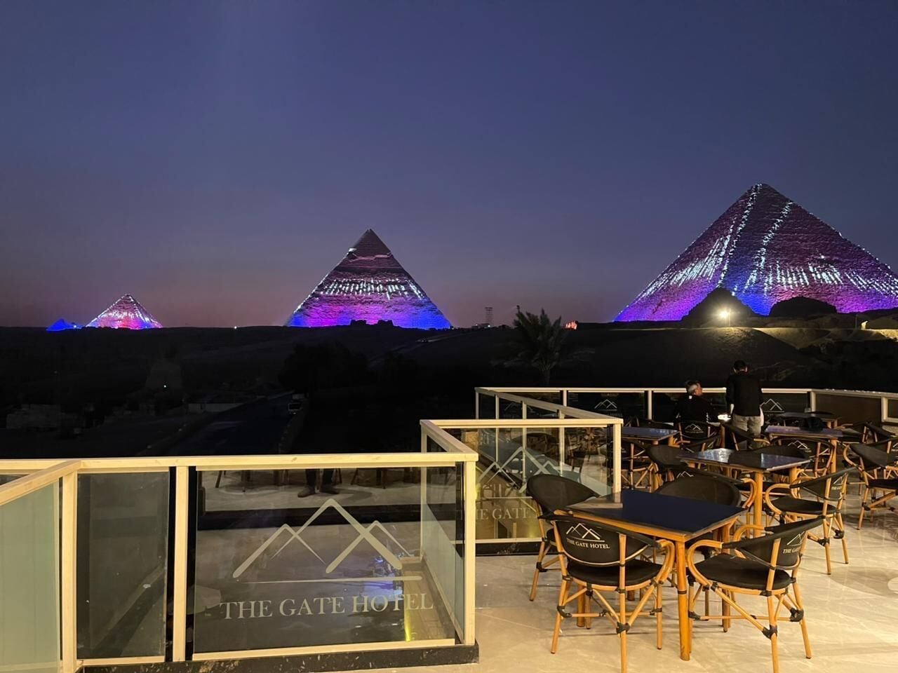 A rooftop terrace with tables and chairs, overlooking pyramids.