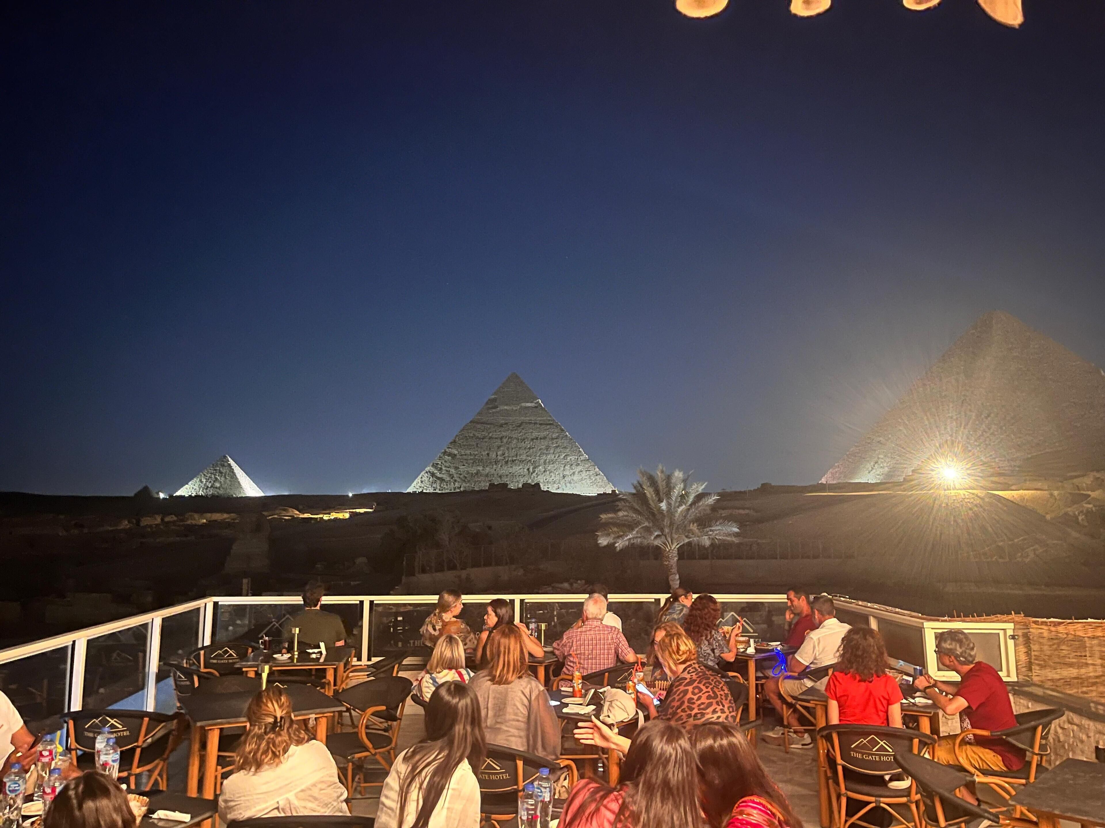 A rooftop dining area with tables and chairs, overlooking pyramids.