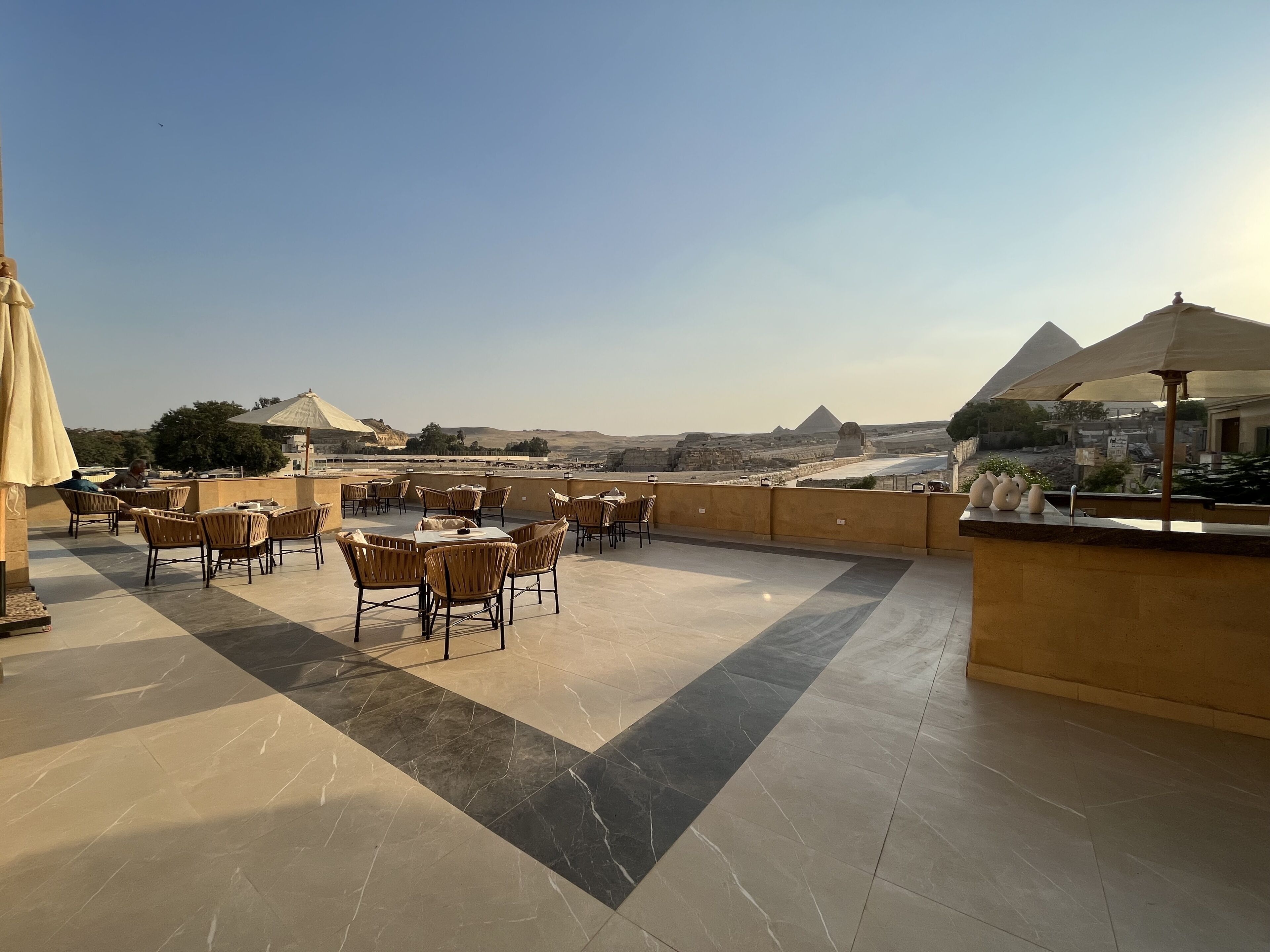 A rooftop terrace with tables and chairs, offering a view of pyramids and desert landscape.