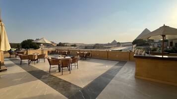 A rooftop terrace with tables and chairs, offering a view of pyramids and desert landscape.