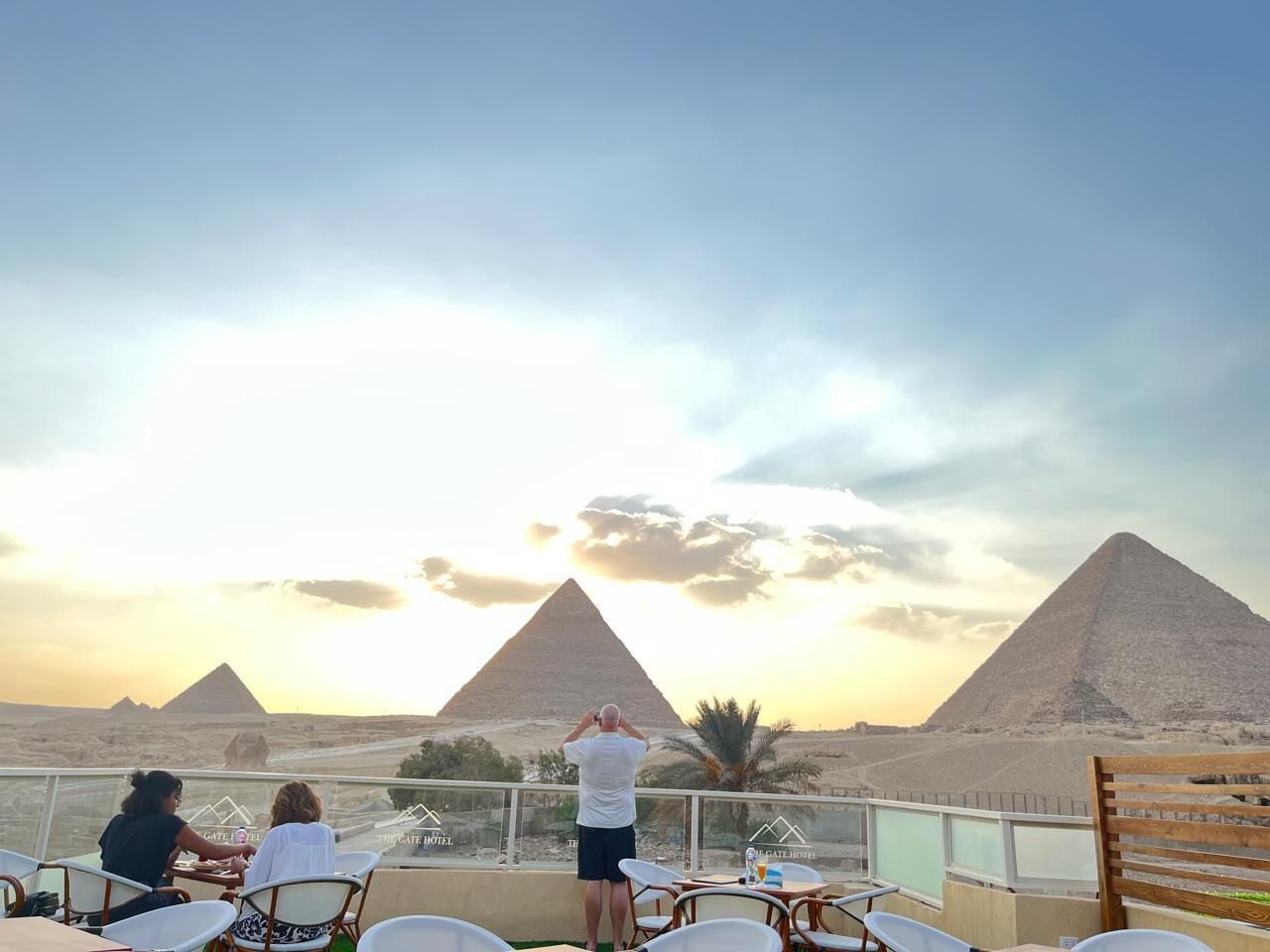 A terrace with a view of the pyramids, outdoor seating, and a railing.
