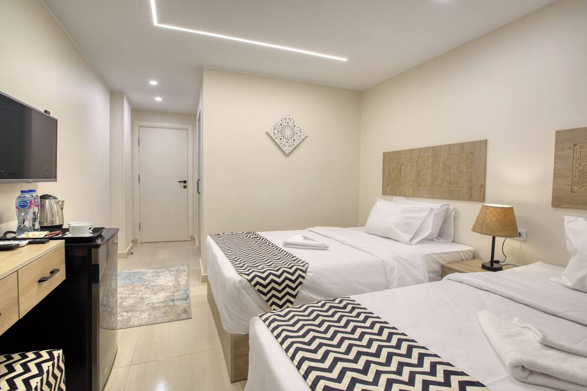 A hotel room with two beds, a desk with a television, a coffee maker, and a wall-mounted artwork.
