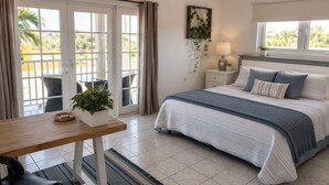A bedroom with a bed, bedside table, lamp, and a view of the outdoors. - Villa Athena GORGEOUS home with large private pool! (Noord)