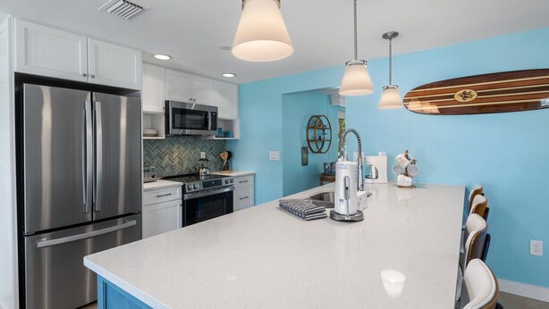 A modern kitchen with stainless steel appliances, a large island, and pendant lighting. - Da Beach House: 2 Blocks to Beach, Pool & Spa by Anna Maria Life Vacation Rentals (Holmes Beach)
