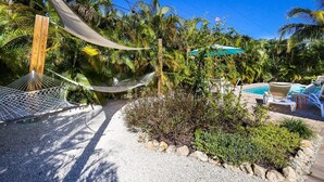 A hammock, a pool, and lounge chairs in a tropical garden setting. - Da Beach House: 2 Blocks to Beach, Pool & Spa by Anna Maria Life Vacation Rentals (Holmes Beach)
