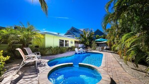 A swimming pool with lounge chairs, a hot tub, and a building in the background. - Da Beach House: 2 Blocks to Beach, Pool & Spa by Anna Maria Life Vacation Rentals (Holmes Beach)
