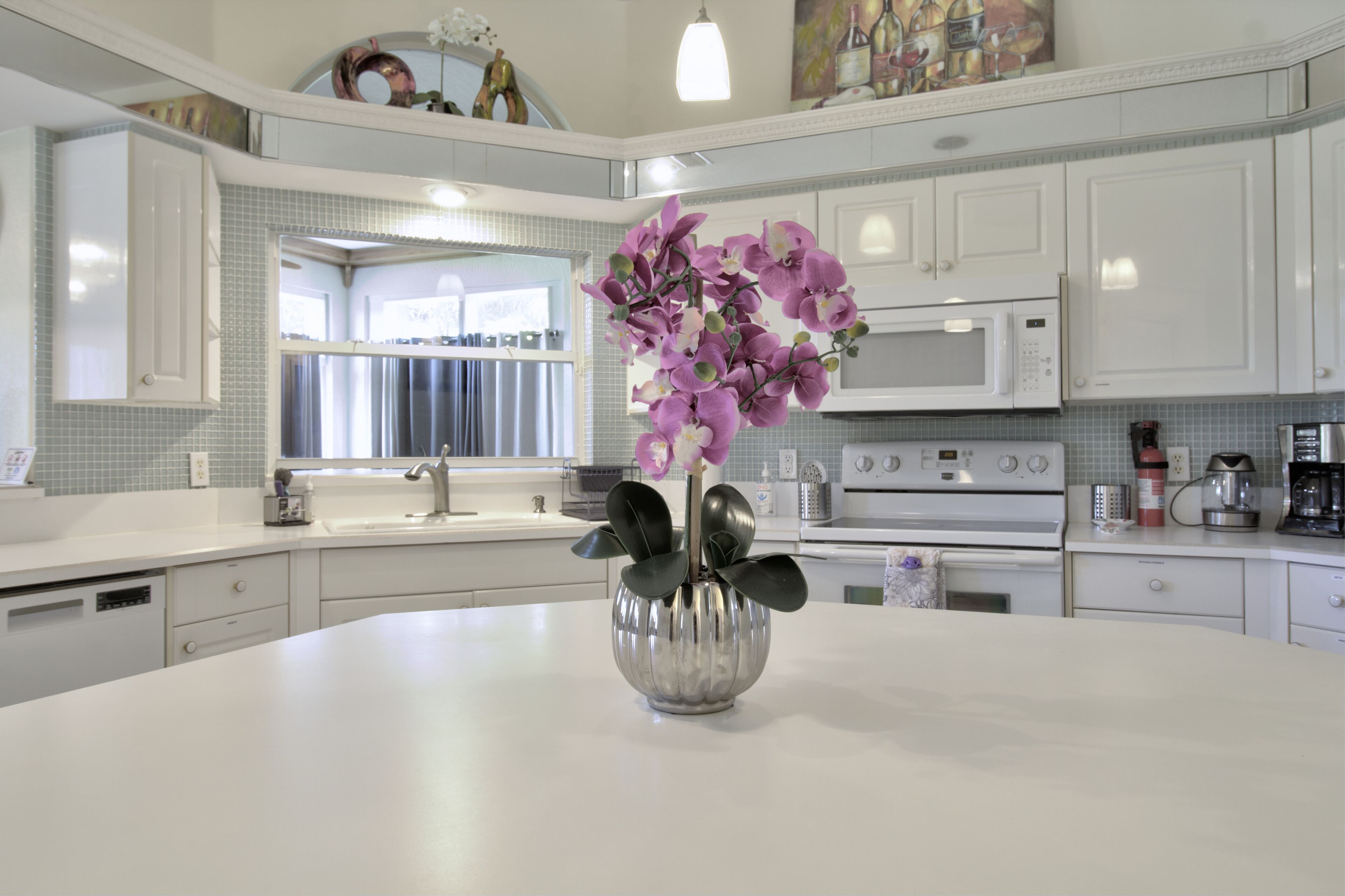 A modern kitchen with white cabinetry, a central island with a vase of purple flowers, and a microwave above the oven.
