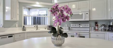 A modern kitchen with white cabinetry, a central island with a vase of purple flowers, and a microwave above the oven.