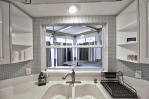 Un baño con lavamanos, espejo y ventana. La ventana ofrece vista a una cancha de tenis.
