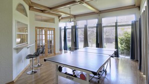 Un'ampia stanza con tavolo da ping pong, due sgabelli da bar e ampie finestre con vista sull'esterno.