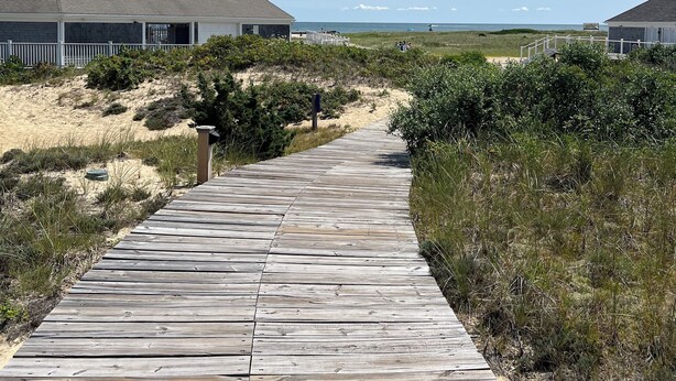 Une promenade en bois menant à des maisons de plage, sous un ciel dégagé.