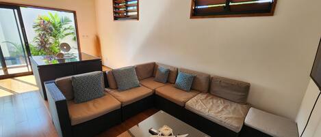 A modern living room with a sectional sofa, a glass coffee table, and a view of the outdoors.