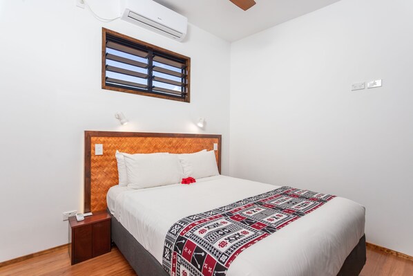 A neatly made bed with a patterned blanket, a wooden headboard, and a small bedside table with a lamp. - Atupa Suites (Rarotonga)