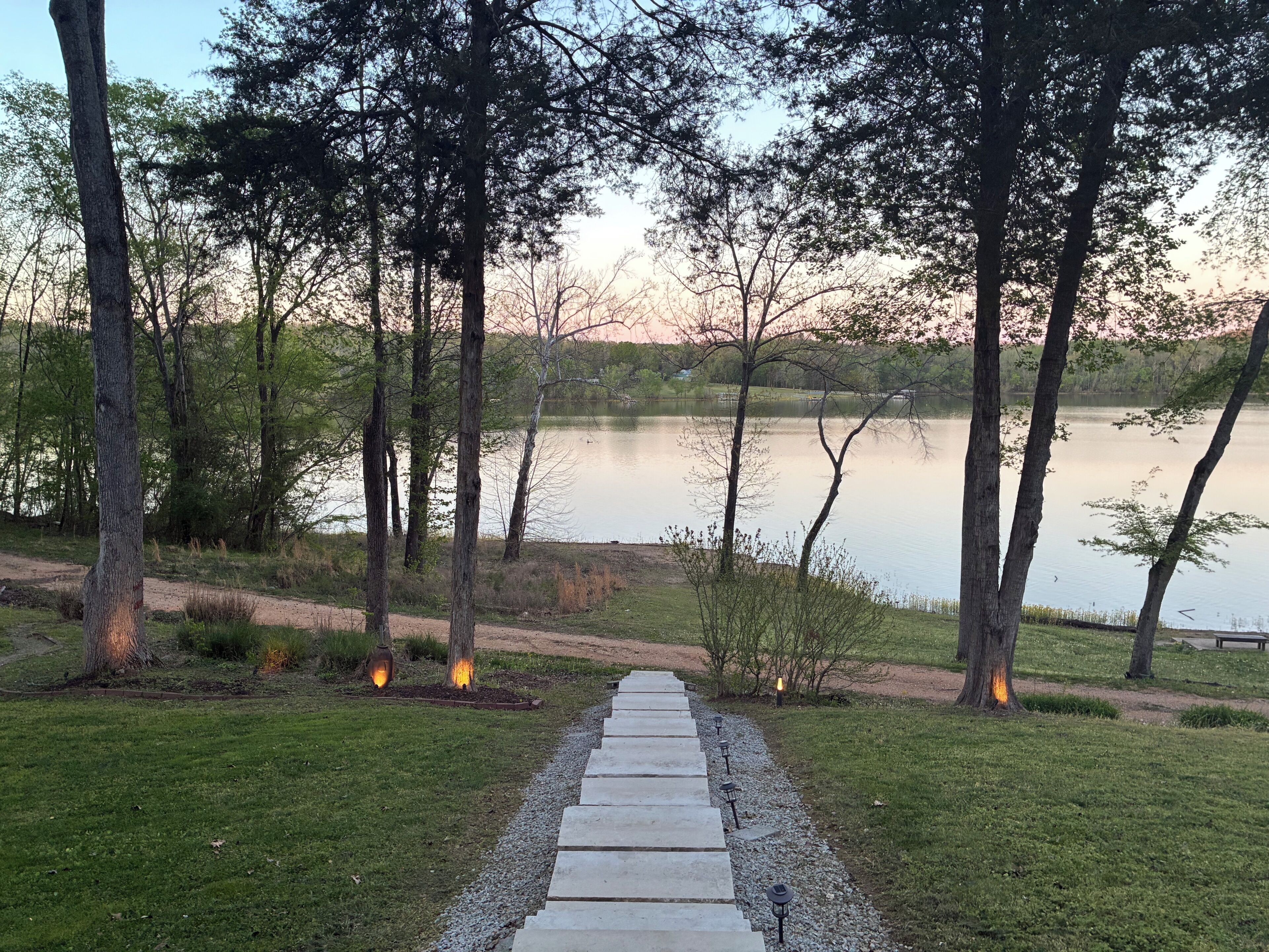 A pathway leading to a lake with trees and a bench.
