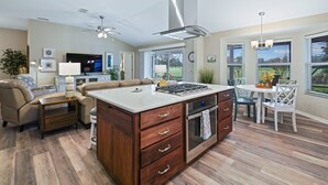 Cozinha moderna com ilha central, forno embutido e área de jantar com mesa e cadeiras brancas.
