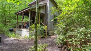 Un chalet rustique doté d’un porche, entouré d’une forêt dense.